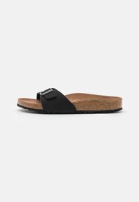 Black slide sandal with a cork footbed, featuring a textured strap and metallic accent. The sole is rubber with a wave pattern for grip.