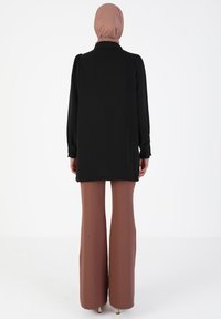 Black long-sleeve tunic with a collar, paired with light brown wide-leg trousers. The fabric appears smooth, with a relaxed fit silhouette.