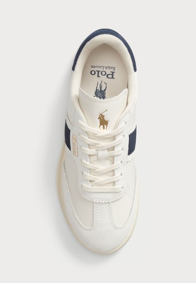 White sneakers with navy accents, textured suede, and smooth leather. Features a lace-up design and a gold logo on the side.