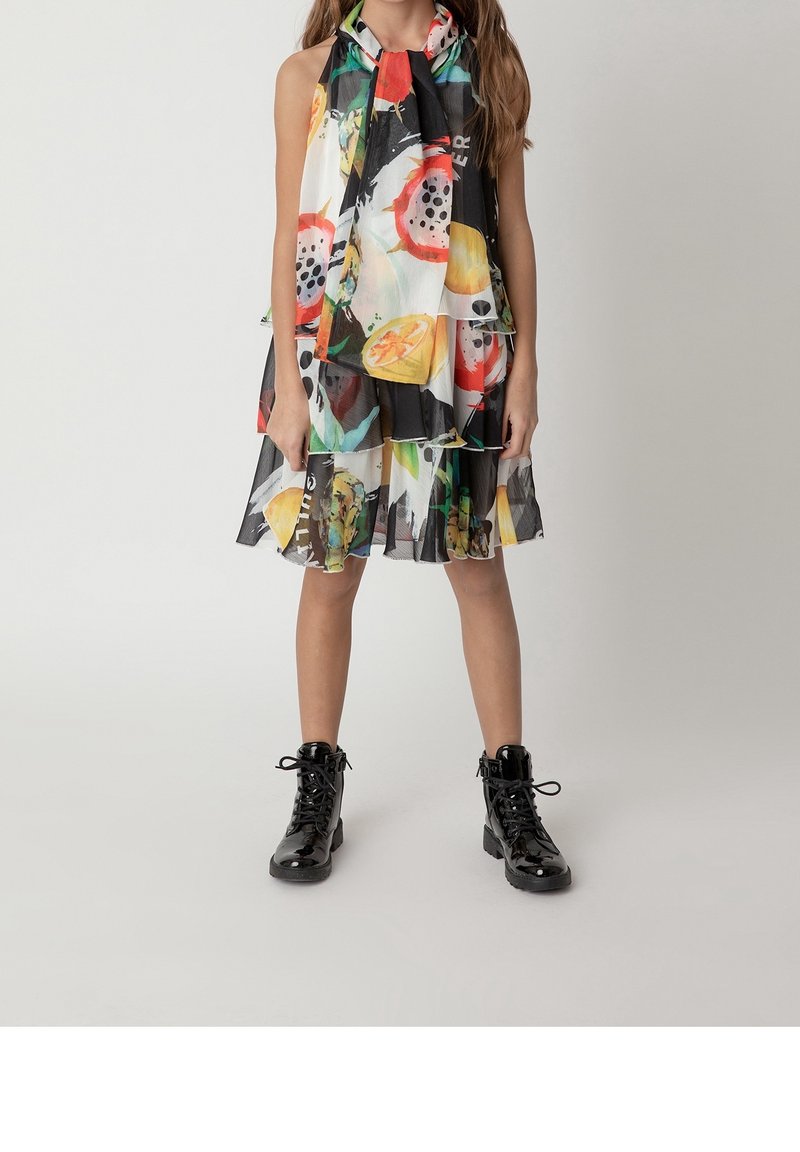 La robe présente un motif fruité multicolore, un tissu semi-transparent, un design à étages et un détail en foulard. Associée à des bottes de combat noires à lacets.