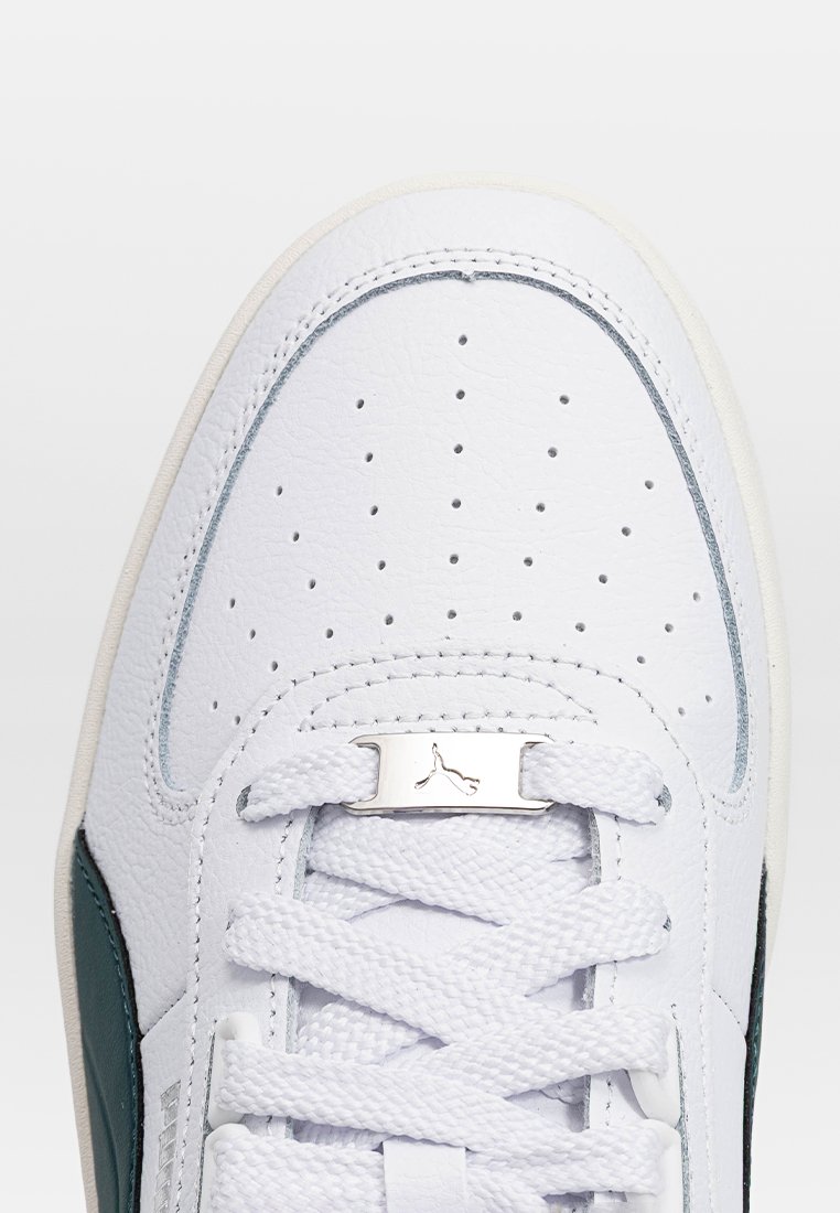 Sneaker in pelle bianca con punta perforata, dettagli verdi, design con lacci e placca logo argentata. Presenta materiali testurizzati e colori a contrasto.