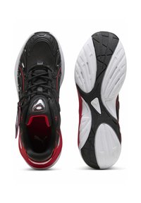 Chaussures de sport noires et rouges avec une tige en mesh, un col rembourré et une semelle blanche présentant des motifs de grip texturés. Accents réfléchissants présents.