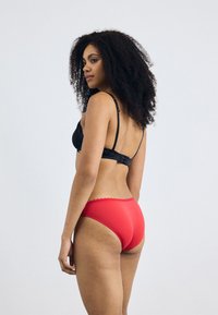 Black lace bra with adjustable straps, paired with red high-waisted briefs featuring scalloped edges. Smooth texture and fitted design.