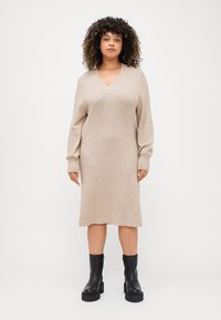Knit bézs színű, hosszú ujjú ruha V-nyakkal, laza szabással, bordás textúrával és térd alá érő hosszúsággal, fekete bokacsizmával párosítva.