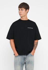 Zwarte katoenen t-shirt met korte mouwen, met witte tekst "VERSPEEL CULTUUR NIET" op de voorkant. Slim fit ontwerp met een ronde hals.