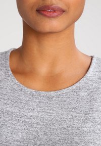 Szary top z tkaniny o gładkiej fakturze i okrągłym dekolcie, odsłaniający skórę tuż poniżej obojczyka. Widoczny delikatny melanż.