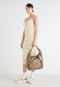 Strick, hellgelides Midi-Kleid mit verstellbaren Trägern und einer vorderen Schleife, kombiniert mit einer braunen Handtasche im Schlangenmuster und klobigen weißen Sneakers.