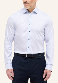 Camicia a righe azzurro chiaro con maniche lunghe, colletto button-down e bottoni scuri. Indossata con pantaloni navy scuri e una cintura nera intrecciata.