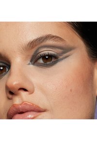 Gros plan sur un visage mettant en avant des yeux marron chaleureux, des sourcils bien dessinés et un teint lisse. Le maquillage des yeux présente des nuances de gris et de beige avec des lignes nettes.