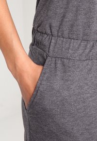 Mono de tela gris con una cintura fruncida, bolsillos laterales y una textura suave, que destaca por su comodidad y diseño casual.