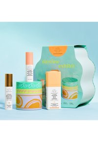 Drunk Elephant daytime skincare set with multivitamin eye cream, hydrating serum, anti-pollution drops, and decorative packaging on blue background.
