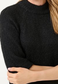 Černý pletený svetr s texturou, vysokým ribetovým límcem a krátkými, zúženými rukávy. Materiál vypadá měkce a útulně.