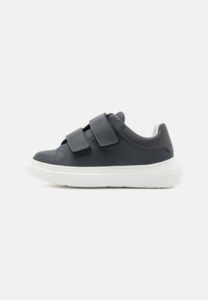 Sneaker grigio con due cinturini in velcro, tomaia in materiale sintetico liscia, suola in gomma bianca, punta tonda e dettagli testurizzati sul tallone.