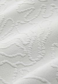 Tela blanca texturizada con un patrón elevado. El tejido es apretado, con áreas suaves y estriadas en contraste que crean profundidad.