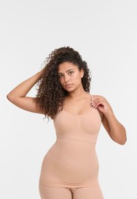Top sin mangas ajustado en tono nude con tirantes delgados, diseño sin costuras, tejido elástico y sutil brillo, diseñado para comodidad y soporte.