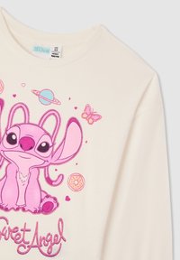 Kremowa koszula z długim rękawem, z różową postacią z kreskówki, otoczoną planetami, motylami i pączkami, z błyszczącym napisem „Sweet Angel”.