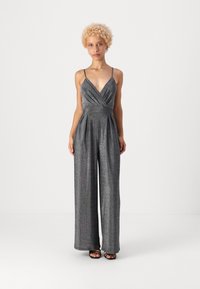 Μεταλλικό γκρίζο φόρεμα με βαθύ V-λαιμό, λεπτές τιράντες, πιεσμένο σχέδιο και φαρδιές παντελόνες. Το ύφασμα έχει μια διακριτική γυαλάδα και βελούδινη υφή.