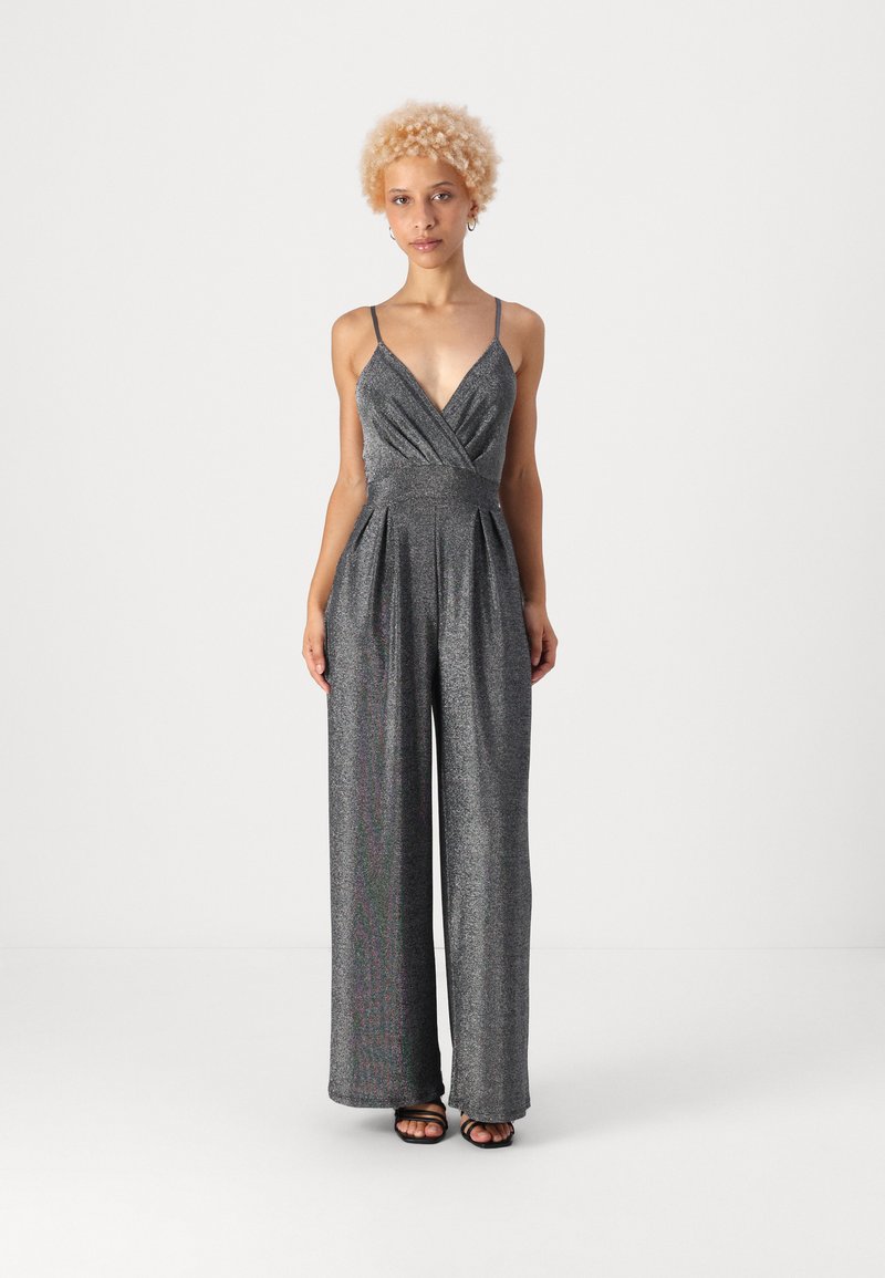 Μεταλλικό γκρίζο φόρεμα με βαθύ V-λαιμό, λεπτές τιράντες, πιεσμένο σχέδιο και φαρδιές παντελόνες. Το ύφασμα έχει μια διακριτική γυαλάδα και βελούδινη υφή.