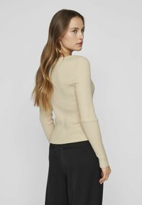 Maglione a maniche lunghe in maglia a coste di un beige chiaro, con scollo rotondo e una silhouette aderente, abbinato a pantaloni larghi neri.