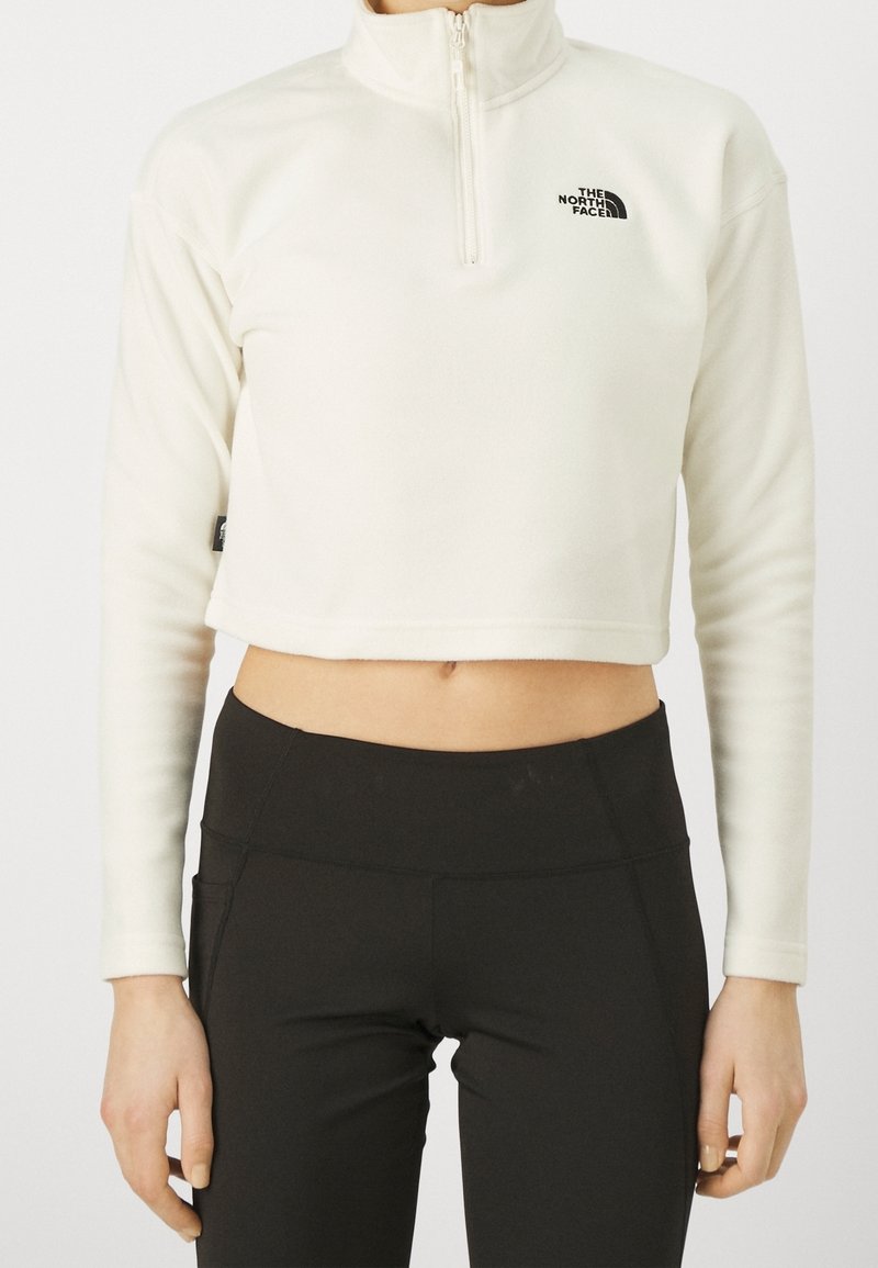 Pullover in pile crema tagliato, con zip a quarti, logo nero sul petto e maniche lunghe, abbinato a leggings neri a vita alta.