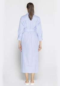 Niebieska i biała, w paski, sukienka koszulowa z długim rękawem i paskiem, wykonana z lekkiego materiału. Posiada kołnierzyk w kształcie szpica oraz zapinane mankiety, sięga poniżej kolan.