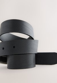 Cinture di pelle nera di larghezze diverse, caratterizzate da una superficie testurizzata e senza parti metalliche visibili. Arrotolate insieme su uno sfondo chiaro.