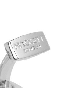 Fibbia in metallo argentato con testo in rilievo "HACKETT LONDON", di forma rettangolare e superficie liscia.
