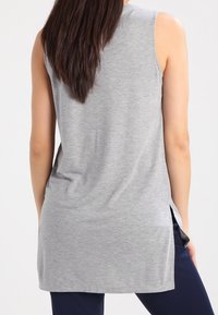 Šedá bezrukávová tunika se bočními rozparky, vyrobená z měkké tkaniny, má volný střih a zaoblený lem, vhodná pro každodenní nošení.