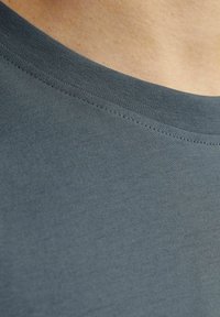Tamsiai mėlynos spalvos marškinėlių audinys su lygia tekstūra, turintis įmegztą apykaklę ir smulkias siūles aplink apykaklę.