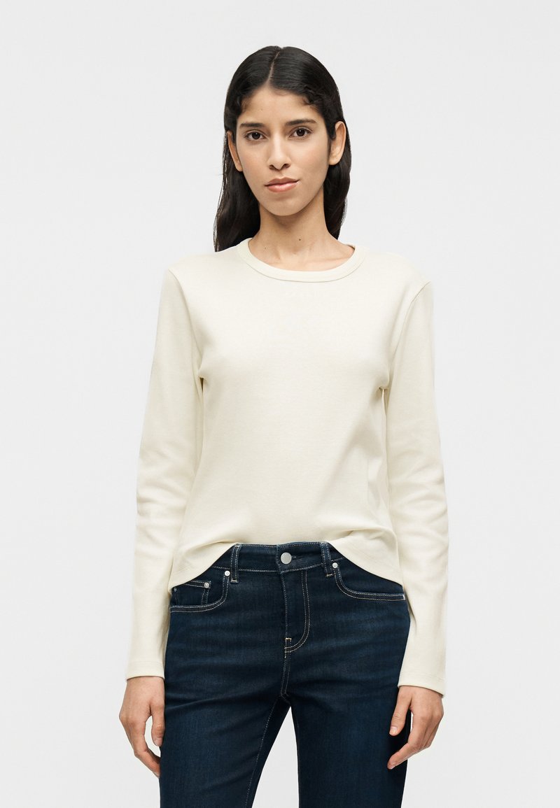 Κρεμ μπλούζα μακρυμάνικη από απαλό βαμβάκι με στ ρογγυλή λαιμόκοψη, συνδυασμένη με σκούρο μπλε τζιν παντελόνι με τσέπες και λεπτομέρειες ραφής.