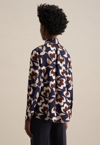 Blusa blu navy con un motivo floreale nei toni di crema e bordeaux. Presenta maniche lunghe, un colletto e una vestibilità rilassata.