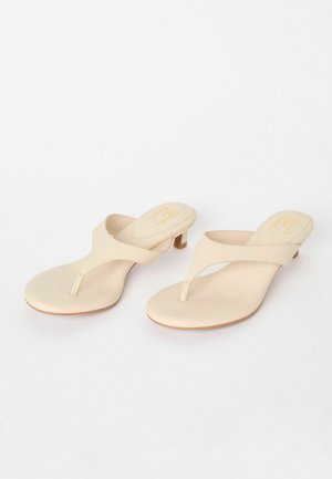Beige tanga sandaler med en glat syntetisk overdel og lille blokhæl. Minimalistisk design med en tæerem og afrundet fodseng.