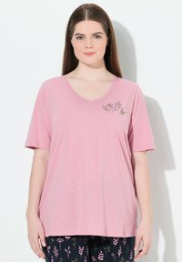 Růžové tričko s krátkým rukávem a v-výstřihem, které má květinový design na levé straně hrudi. Vyrobeno z měkké tkaniny s uvolněným střihem.