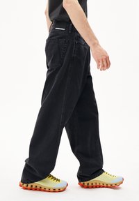 Jean en denim noir avec une coupe droite et des poches arrière visibles, portés avec des baskets colorées au semelle texturée et tige en tricot.