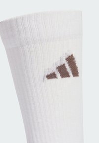 Hvid atletiksok med ribbet struktur, der har en brun strikket tre-stribet logo nær toppen. Blødt stof, midt på læggen længde.