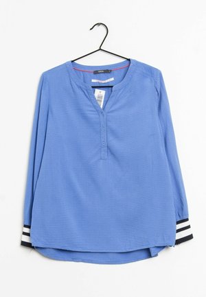 Blue long-sleeve blouse with round neckline, three front buttons, black and white striped cuffs, hanging on a black hanger with price tag.