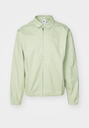Light green jacket made of smooth fabric, featuring a collared neck, front zipper, elastic cuffs, and a subtle logo on the chest.