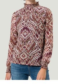 Blouse à manches longues avec un col froncé haut, présentant un motif géométrique vibrant et complexe en violet, marron et crème. Poignets élastiques.