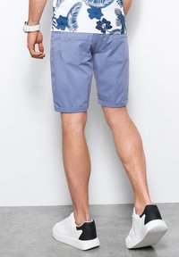 Pantaloni blu chiaro con orli risvoltati e due tasche posteriori, abbinati a sneakers bianche con accenti neri. Combinati con una camicia a fantasia.