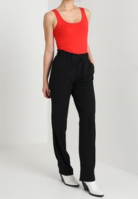 Röd rutmönstrad linne kombinerat med svarta, löst sittande byxor med dragsko i midjan, komplett med vita klackade anklarstövlar.