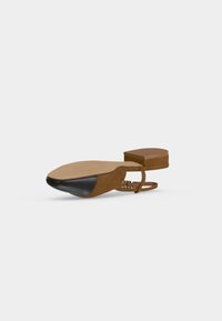 Barna lapos szandál bokapánttal és fekete texturált orr-résszel, talpról és oldalnézetből, egyszerű háttér előtt.