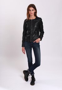 Black leather jacket featuring a zip closure, two front zippered pockets, and a round neckline, paired with blue jeans and black boots.