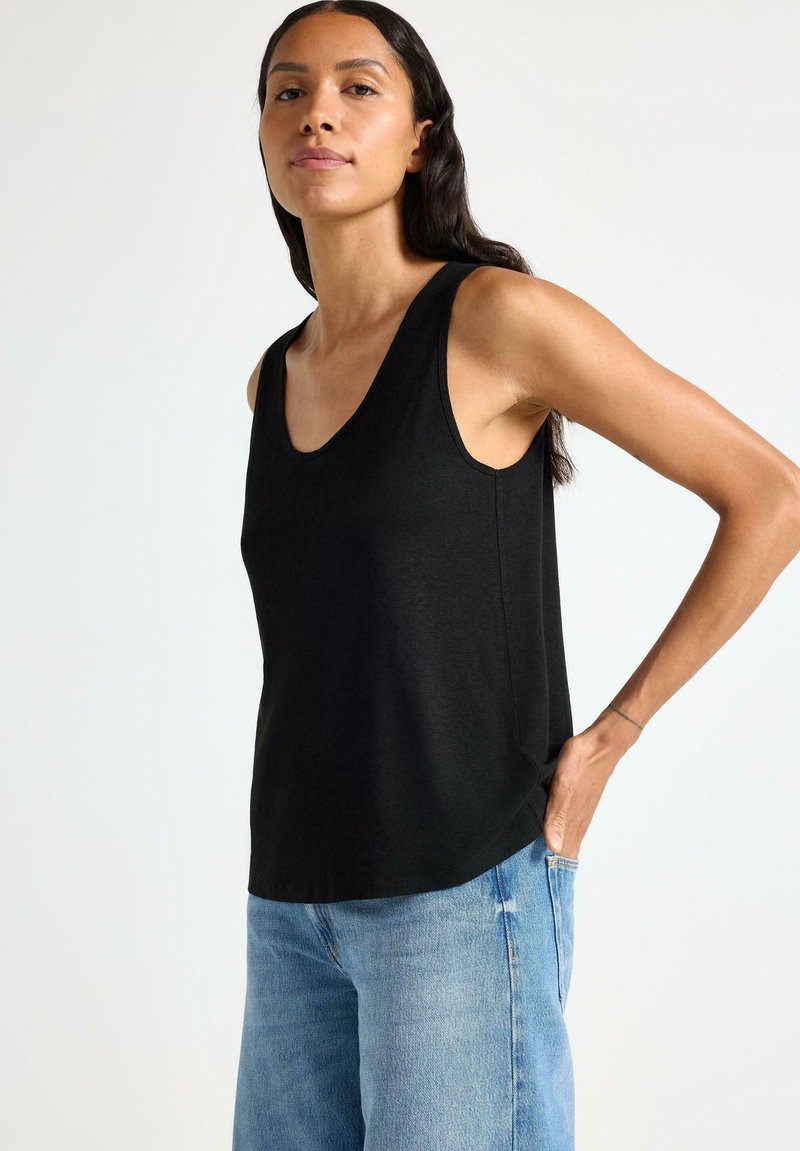 Schwarzes ärmelloses Tanktop mit einem runden Halsausschnitt, kombiniert mit hellblauen, verwaschenen Jeans. Der Stoff wirkt weich und lässig im Stil.