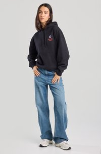 Black cotton hoodie with "SILVER STATE" logo in red, paired with wide-leg, light blue denim jeans, and white sneakers.