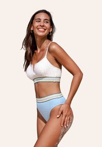 Top bikini bianco con texture e dettaglio a chiave frontale, abbinato a slip a vita alta di colore blu chiaro con strisce multicolori.