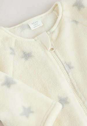 Combinaison en molleton crème pour bébé avec fermeture éclair, ornée de motifs d'étoiles grises dispersés et d'un col côtelé. Tissu doux et texturé.