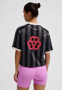 Svart och grårandig tröja med korta ärmar och vit krage, med en stor röd hjärtformad logotyp på baksidan. Matchad med rosa shorts.