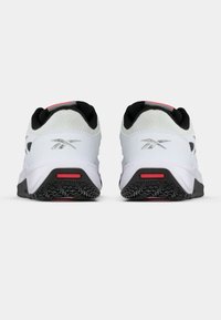 Baltas sporta kurpes ar teksturētu tīkliņa augšdaļu, melniem akcentiem un gumijas zolēm ar sarkanu dizaina elementu papēžā.