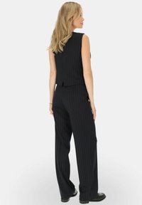 Czarna kamizelka w paski bez rękawów oraz dopasowane spodnie o szerokich nogawkach. Tkanina ma gładką strukturę, dopasowany krój i subtelny połysk.