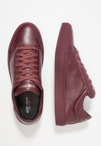 Maroon leather sneakers with textured side panels, round toe, lace-up design, and rubber soles. Features subtle branding on the tongue.